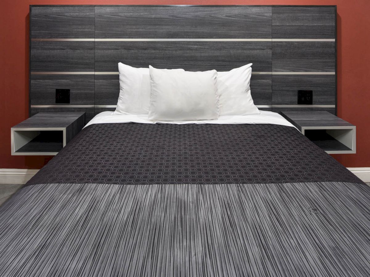 A neatly made bed with white pillows, a black and gray striped bedspread, and a gray headboard against a red wall, with side tables.