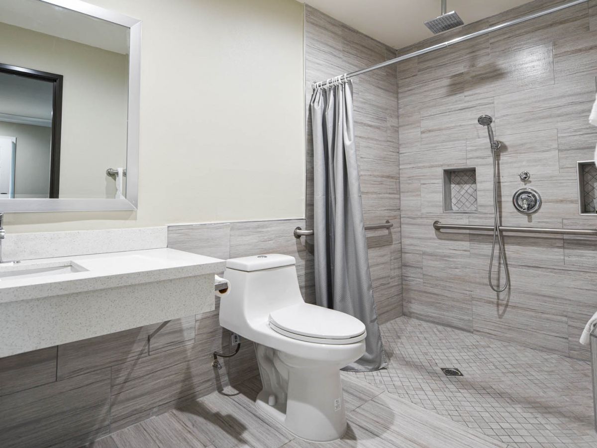 The image shows a modern bathroom with a shower, toilet, sink with a mirror, and a towel hanging. The design is sleek and minimalist.