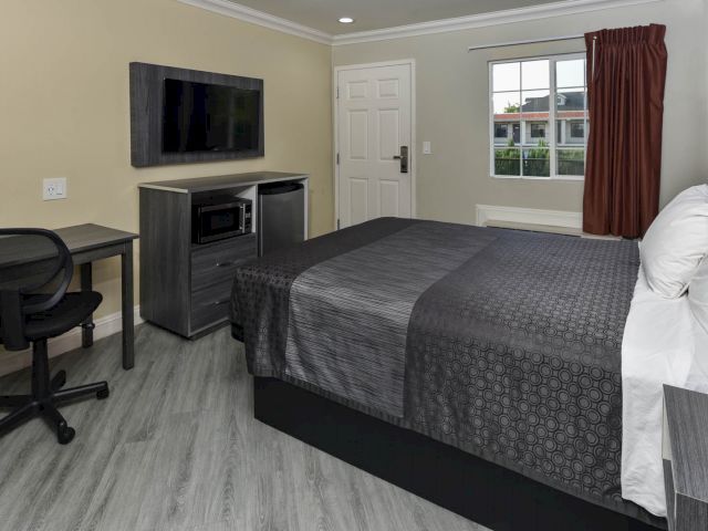 A hotel room with a bed, desk, TV, and window