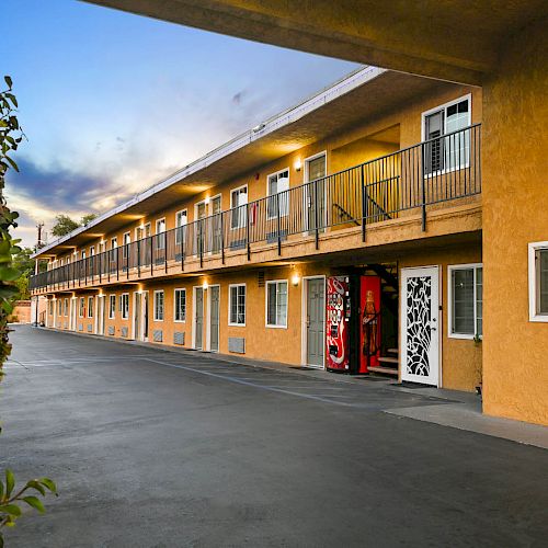 The image shows a two-story motel with a yellow exterior, black railings, and a vending machine visible near a white decorative door.