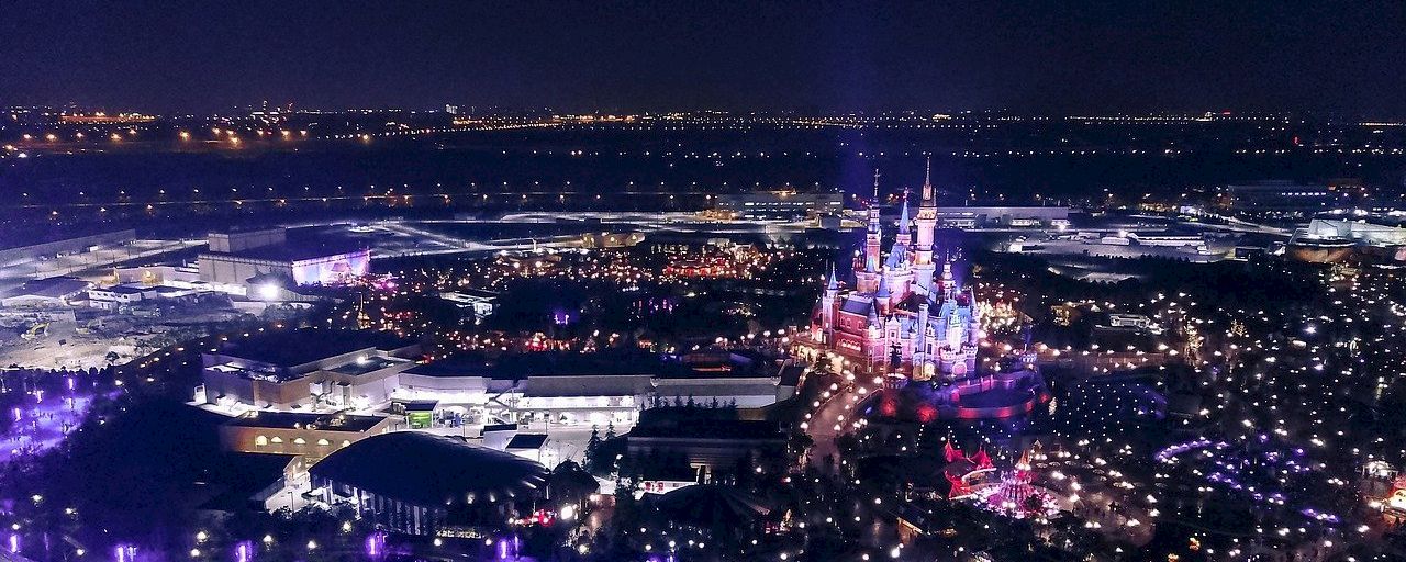 An aerial nighttime view of a city with a prominent castle in the center.