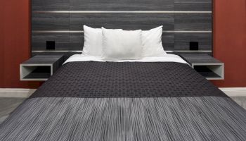 A neatly made bed with white pillows and a dark gray bedspread, set against a wooden headboard and red wall, with two floating bedside tables.