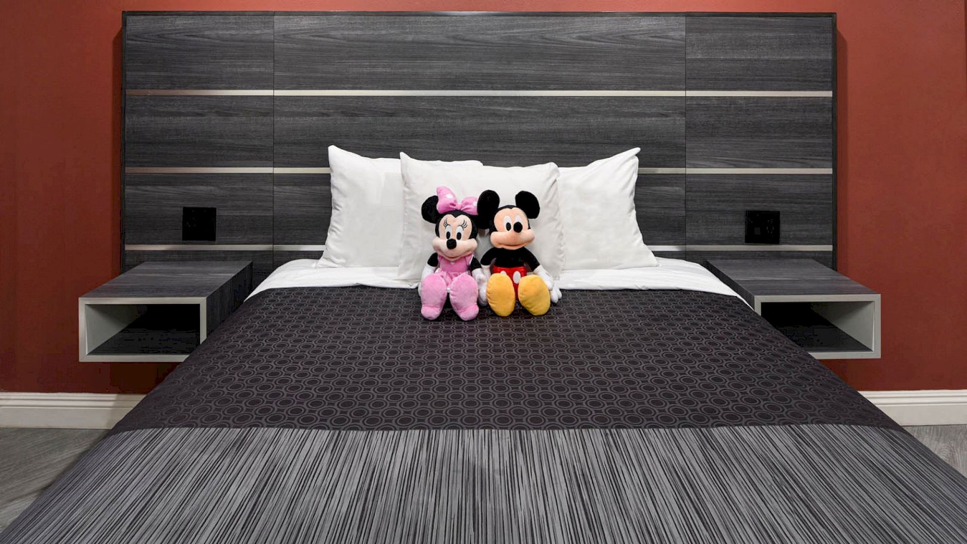 A modern bed with a grey and black headboard features a black and grey striped bedspread, white pillows, and two stuffed toys on the bed.