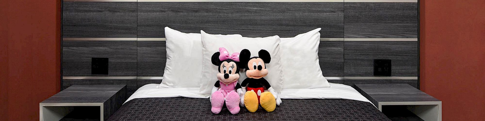 A modern bed with a grey and black headboard features a black and grey striped bedspread, white pillows, and two stuffed toys on the bed.