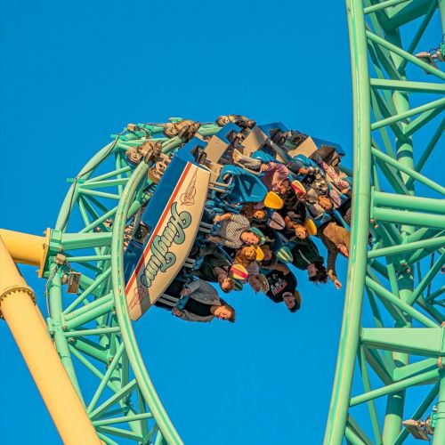 A roller coaster is shown mid-loop with riders holding on tightly and enjoying the thrill against a clear blue sky background.