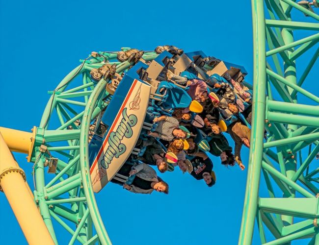 A roller coaster is shown mid-loop with riders holding on tightly and enjoying the thrill against a clear blue sky background.