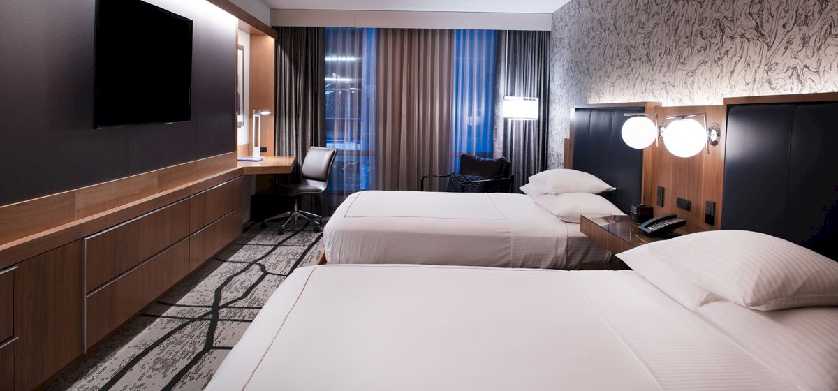 A hotel room with two twin beds, a desk, and a TV on the wall.