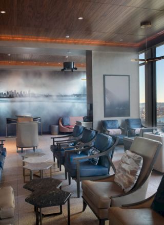 A modern lounge area with comfortable seating, large windows offering a scenic view of a waterfront and a Ferris wheel, and ambient lighting.