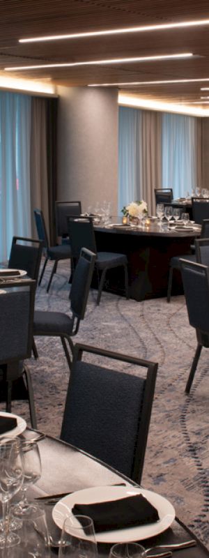 A spacious, elegantly decorated banquet hall with round tables set for a formal event, featuring black tablecloths, white plates, and gold candle holders.