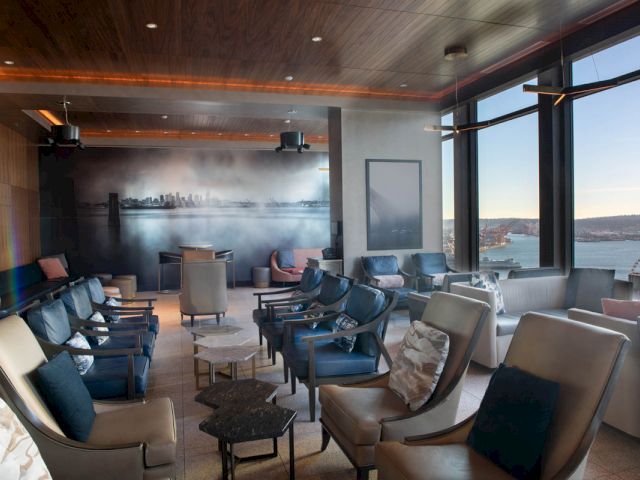 A lounge with comfortable seating and large windows showing a city view.