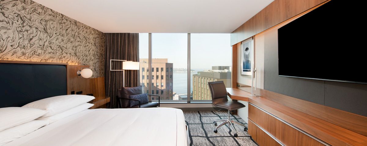 A hotel room with a large bed, desk, chair, and city view.