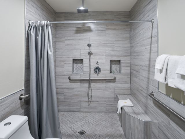 A clean and modern bathroom with a walk-in shower, grab bars, and a bench.