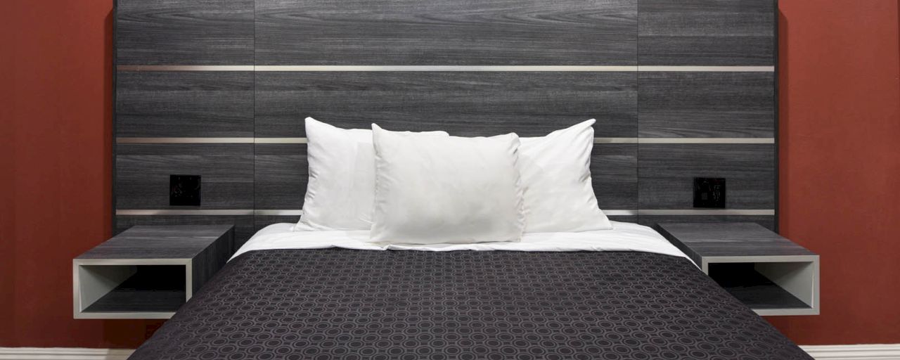 A neatly made bed with white pillows and a dark comforter against a gray headboard with red walls