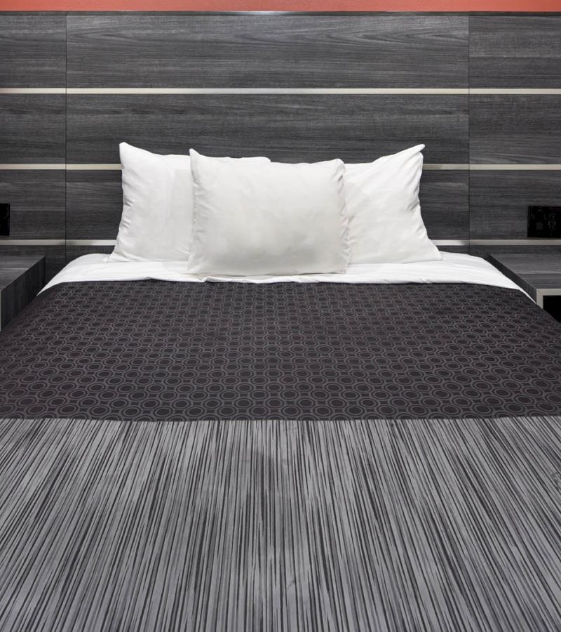 A neatly made bed with white pillows and a dark patterned blanket